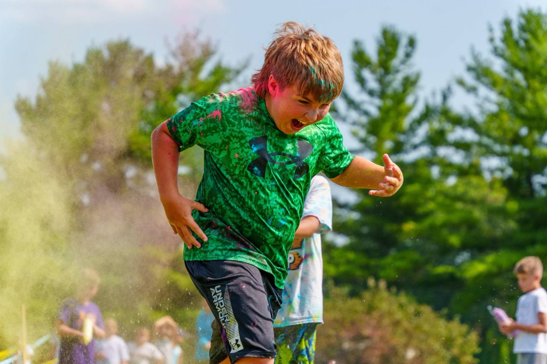 A laughing boy covered in color powder running through a cloud of color at the Color Run