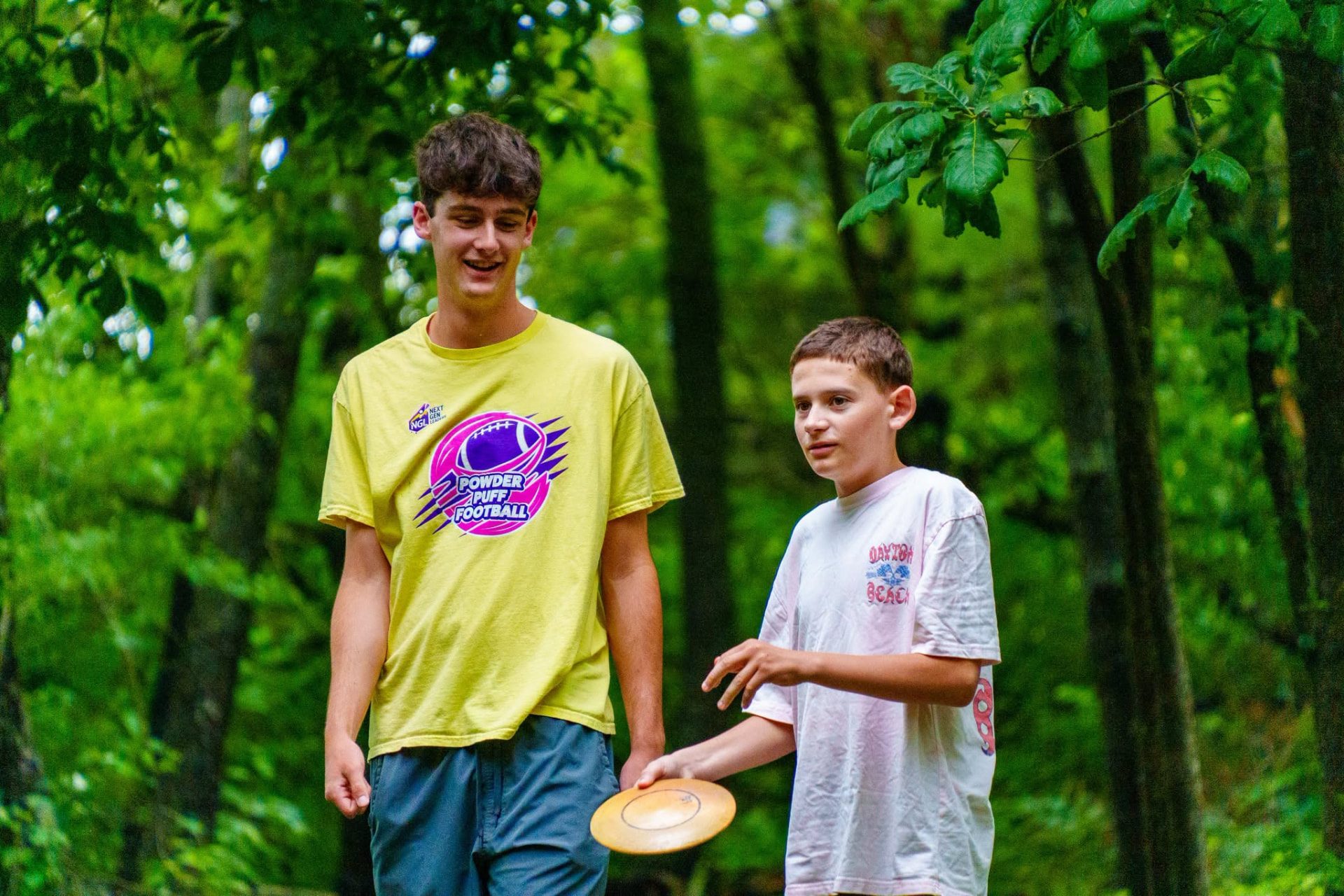 An older teen leader walking a wooded disc golf course with a younger participant